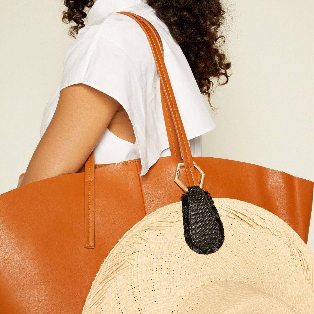 Stylish woman holding a large brown tote bag with a straw hat attached, showcasing a chic summer look.