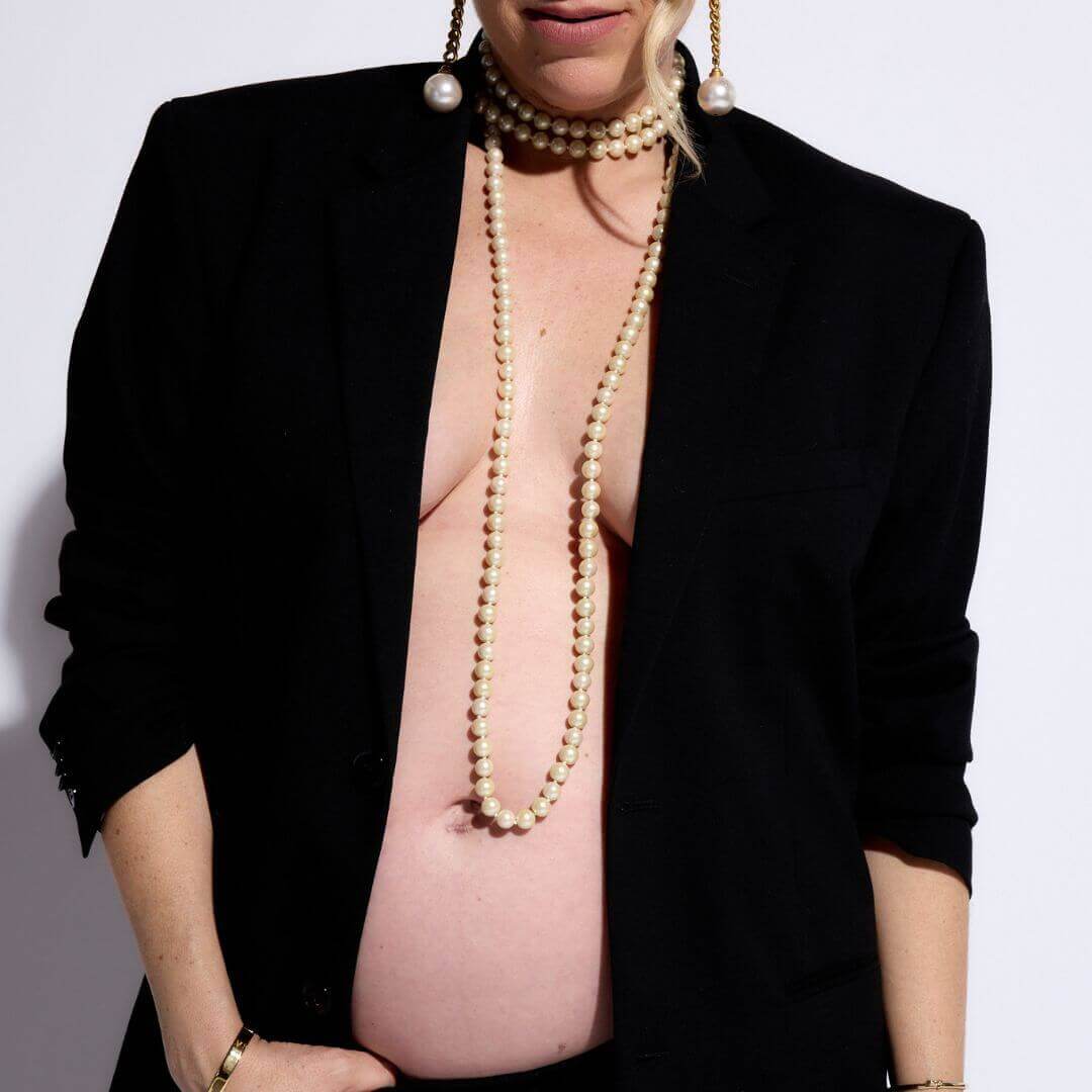 Pregnant woman wearing a black blazer and pearl necklace, showcasing her baby bump in a stylish maternity photoshoot.