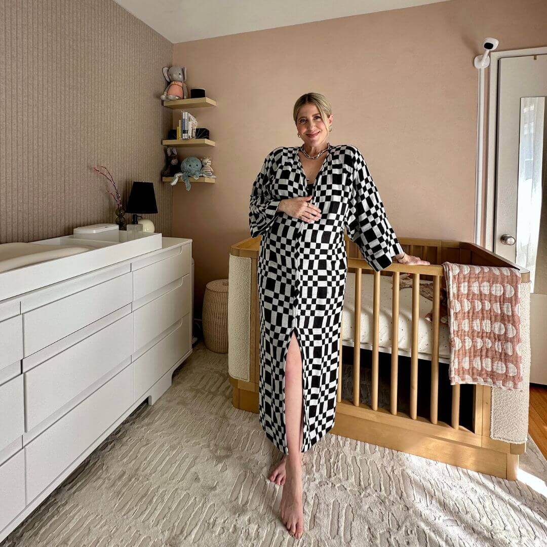 Woman in checkerboard dress standing by a stylish baby crib in a beautifully designed nursery.
