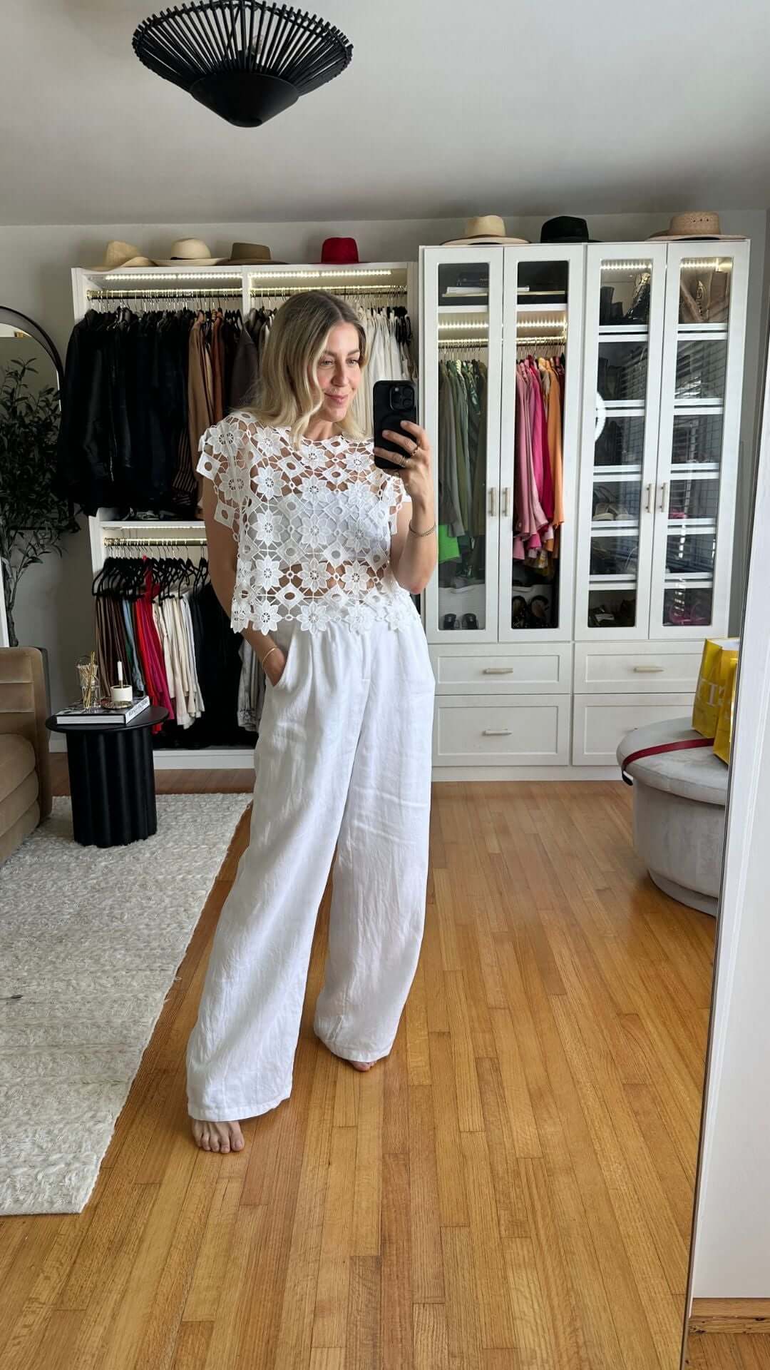 Woman modeling a stylish white lace top and linen pants in a trendy closet setting.