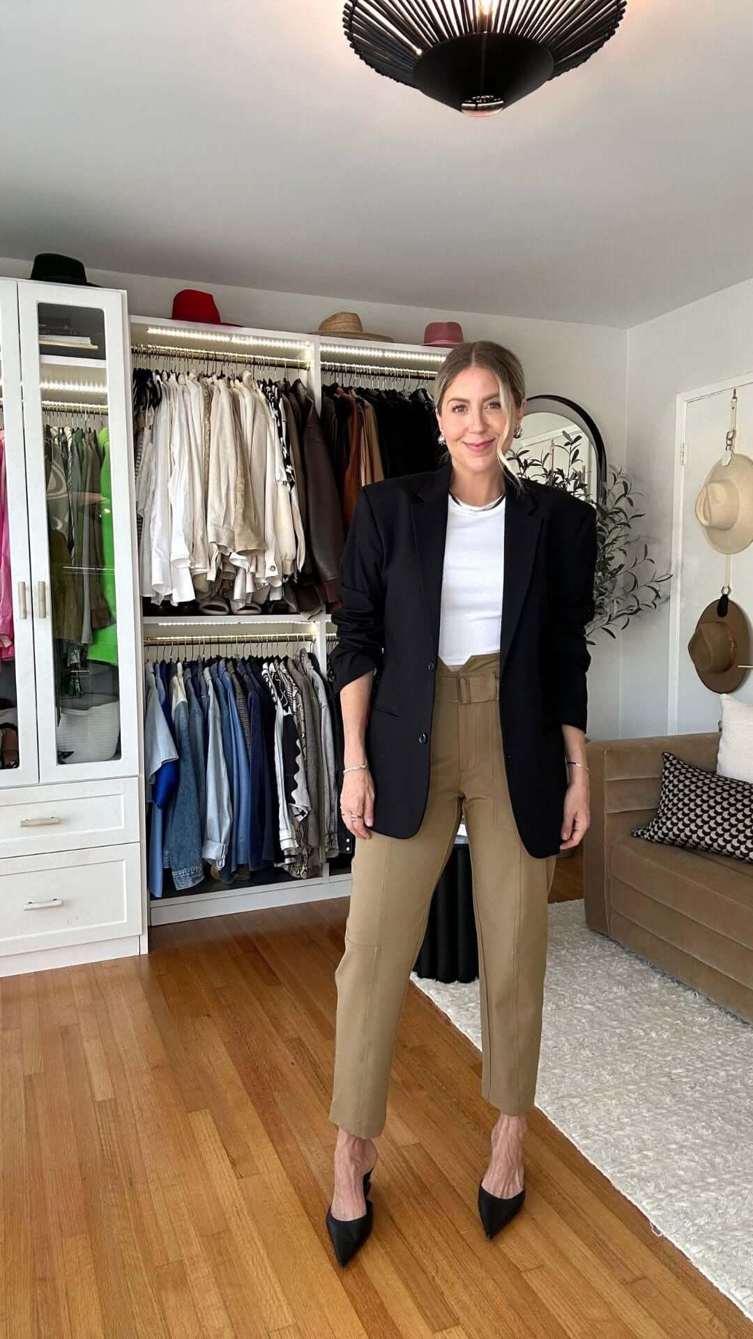 Woman in stylish outfit with blazer and tan pants standing in a stylish closet with clothing racks.