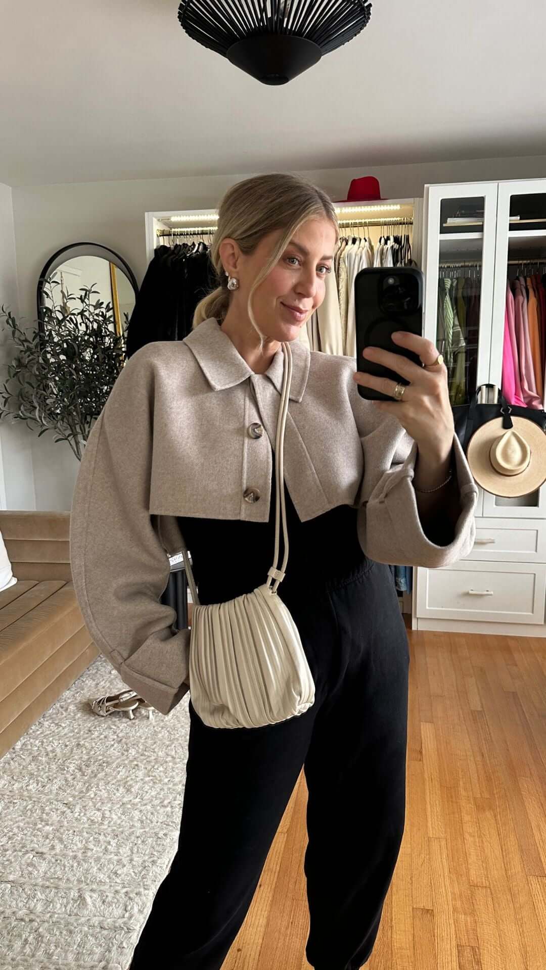 Stylish woman in a cropped sweater and wide-leg pants posing with a small handbag in a bright room.
