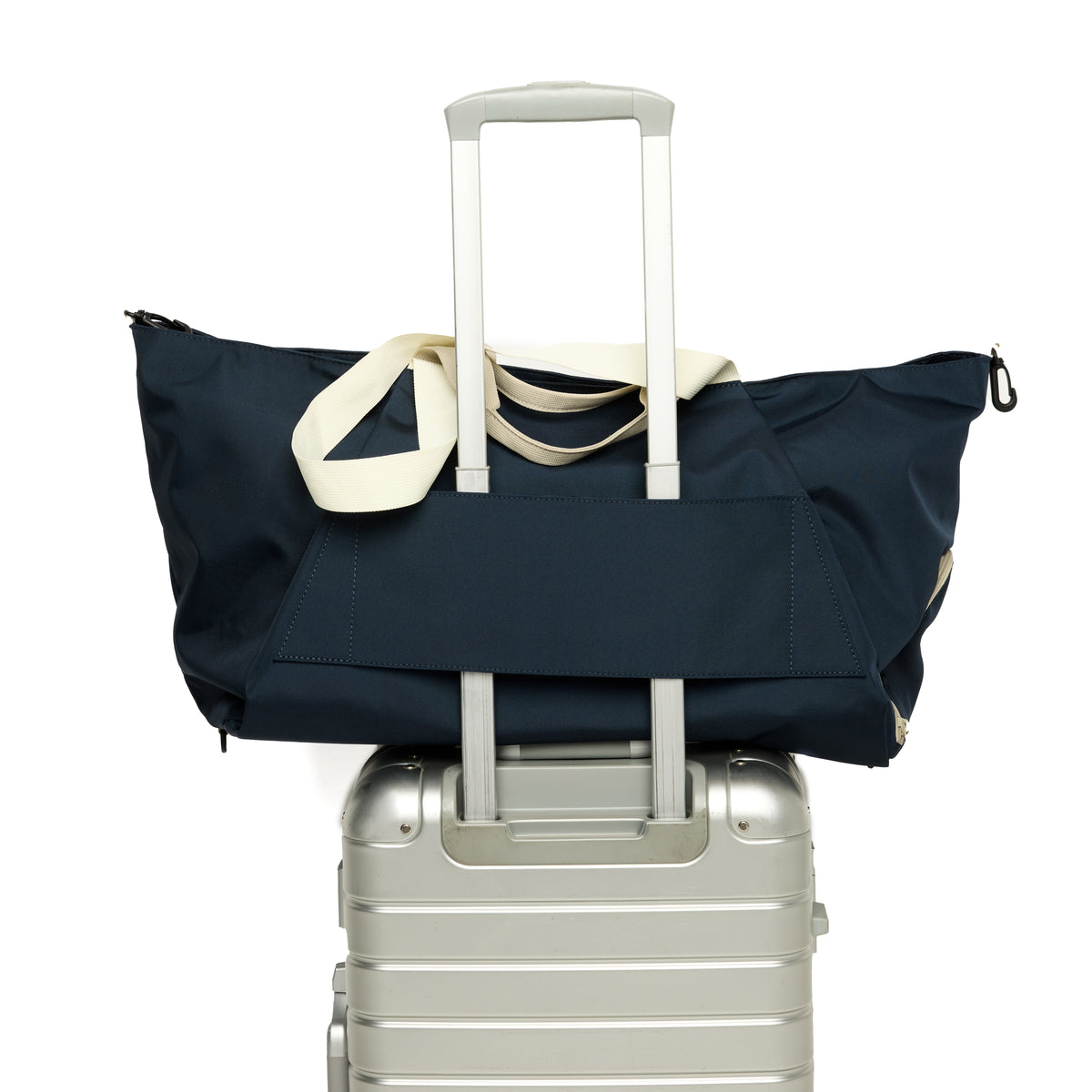 Navy duffel bag with white handle draped over a silver suitcase on a white background