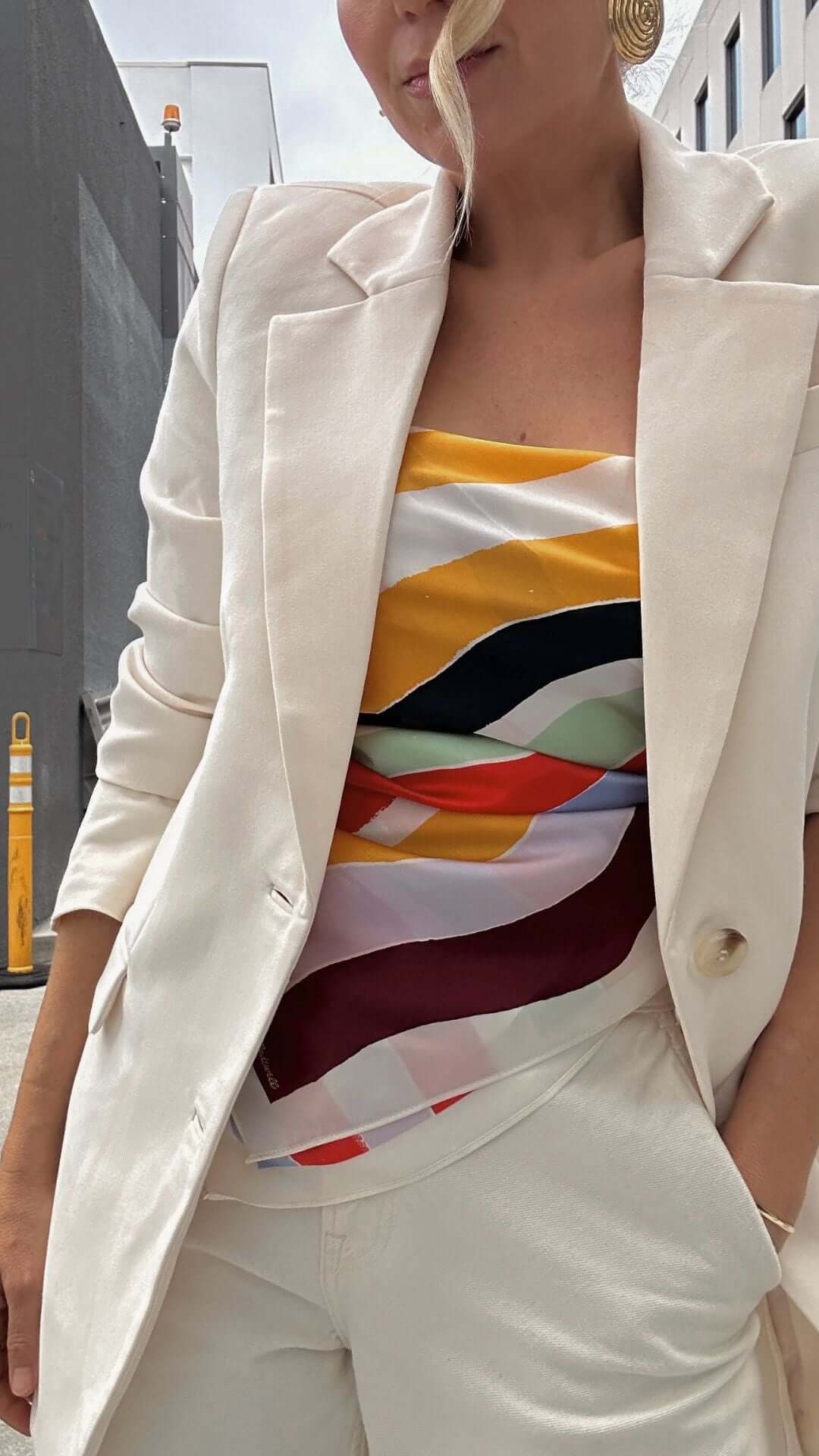 Model wearing a white blazer and colorful striped top, showcasing a chic summer outfit in an urban setting.
