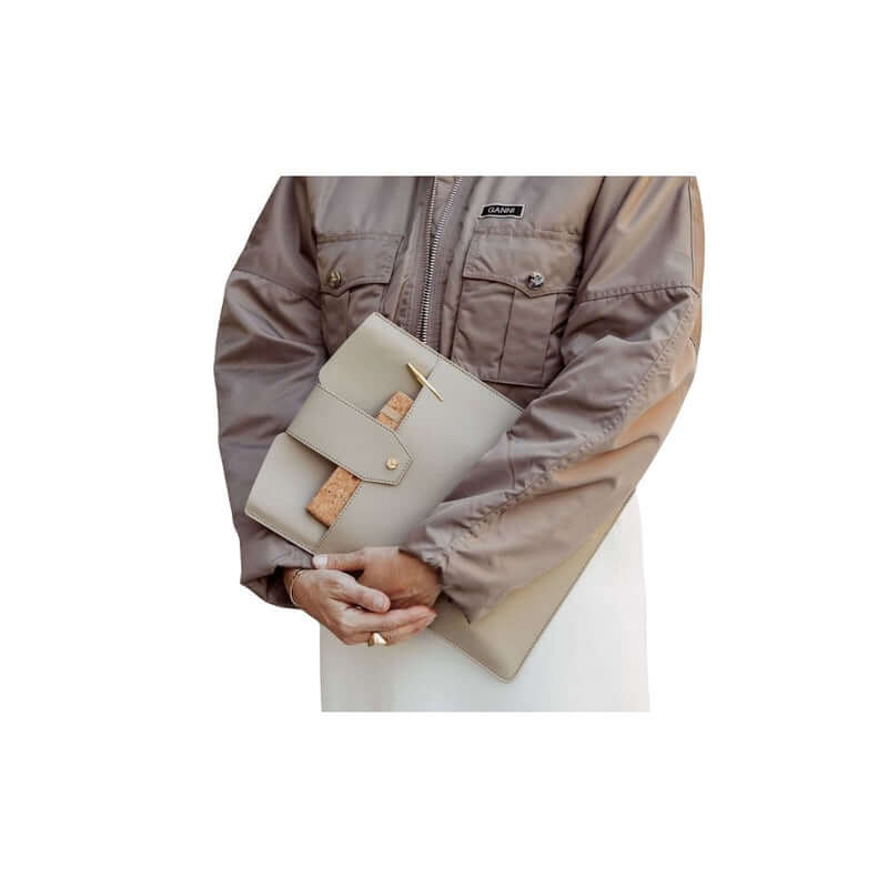 Stylish person holding a modern beige clutch with a unique buckle detail, dressed in a cozy brown jacket.