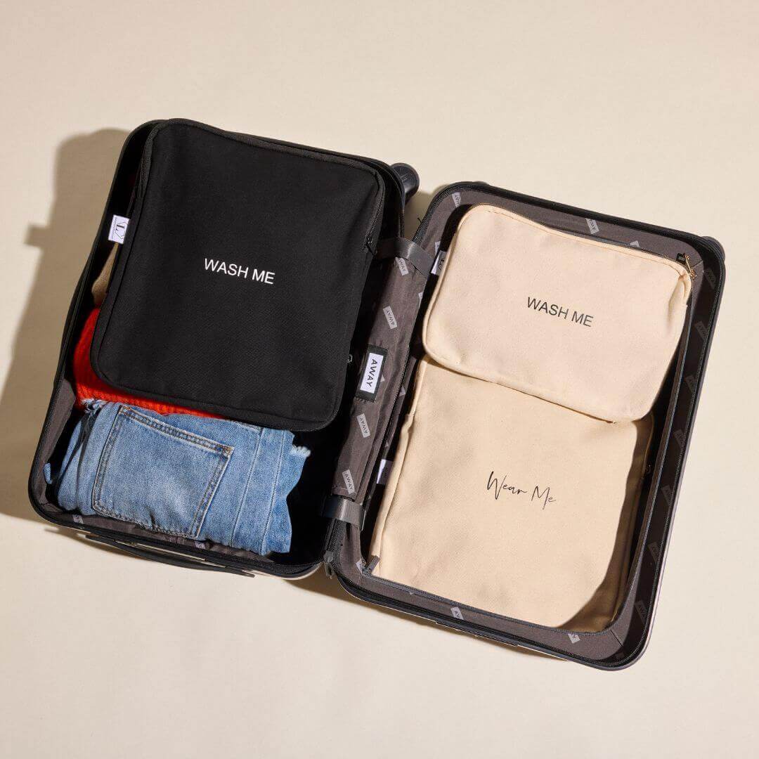 1 black and 2 natural laundry bags. on top of clothes in a black suitcase.