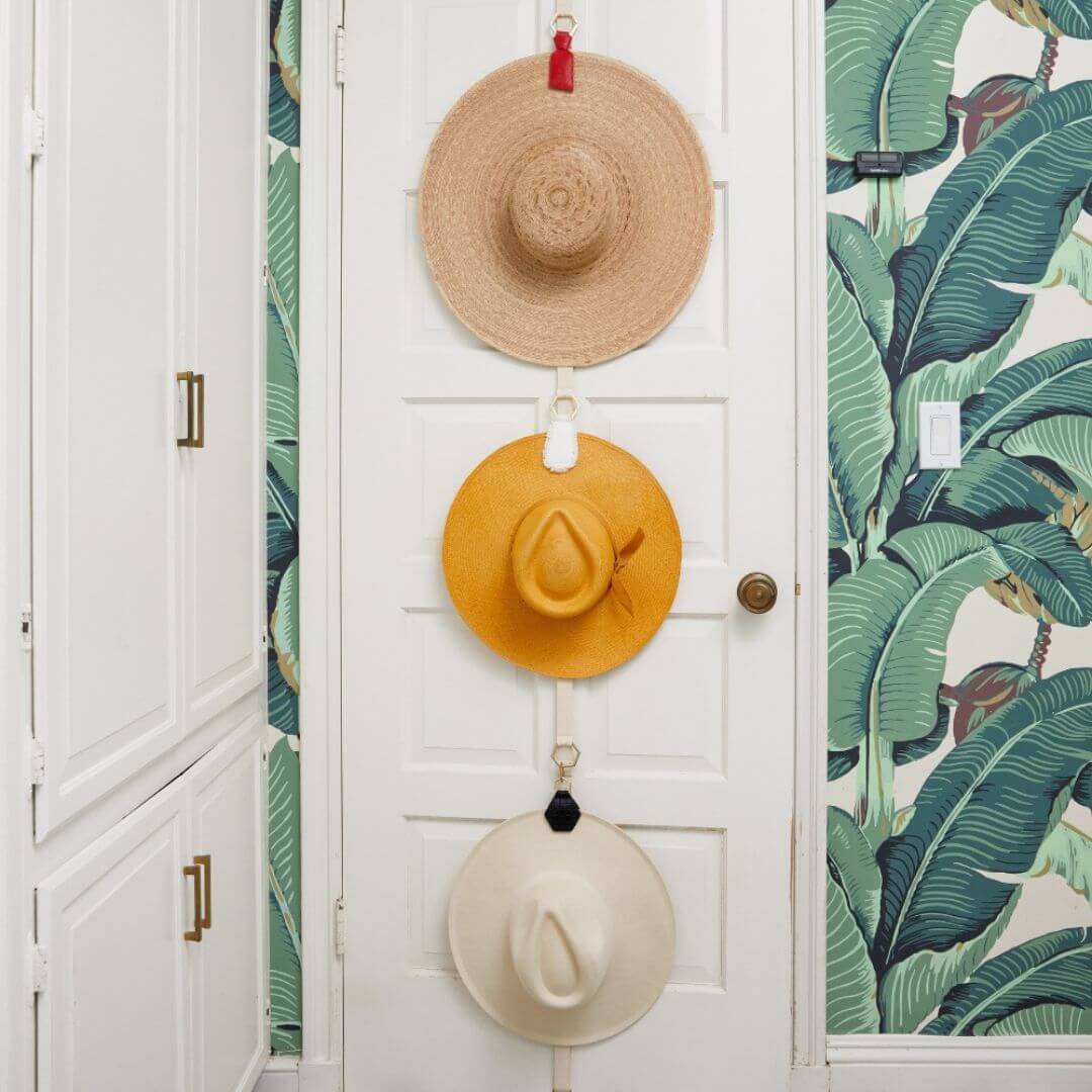 Stylish hats organized on a door using The Collector Hat Organizer, featuring natural, yellow, and white hats.
