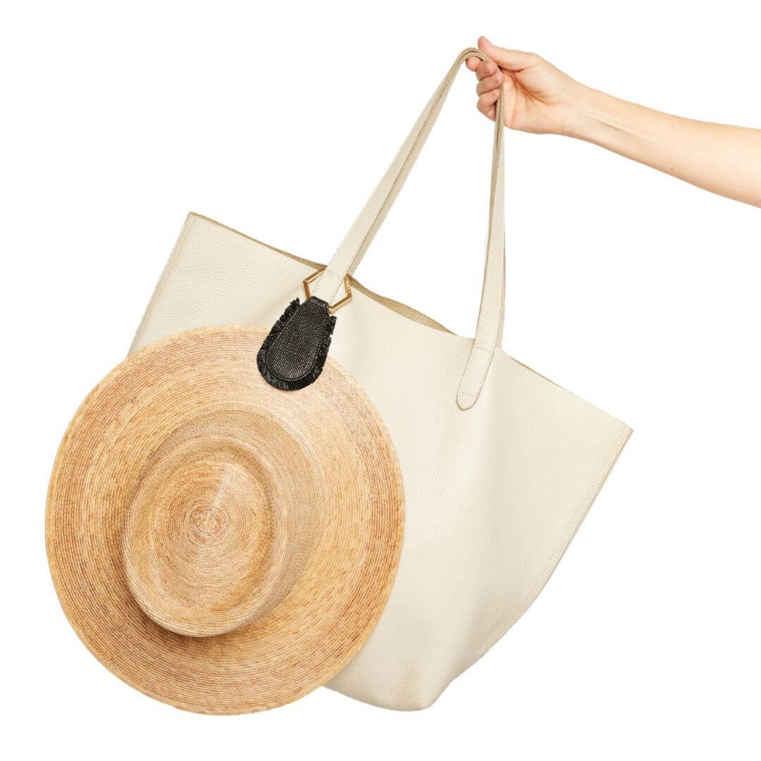 The Fray TOPTOTE hat clip with raffia trim holding a straw hat on a beige tote bag