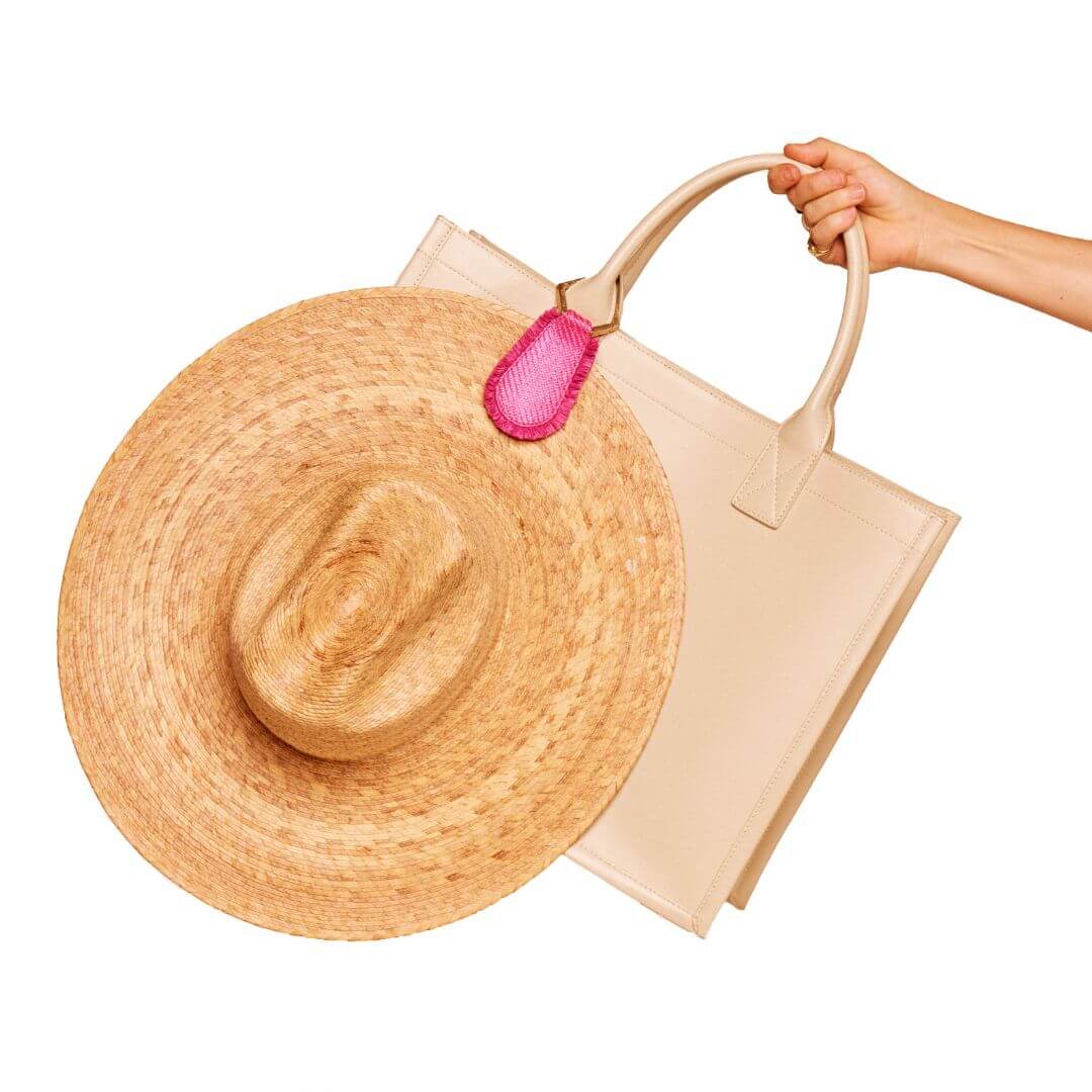 The Fray TOPTOTE Hat Clip with raffia trim holding a straw hat on a beige handbag.