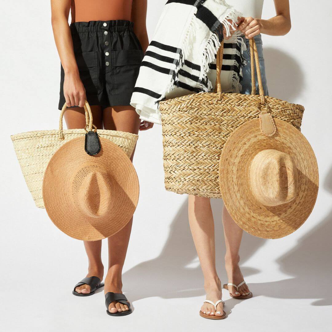2 women in shorts holding natural straw tote bags, one with TOPTOTE Fray Natural holding a cream straw hat, the other TOPTOTE Fray Black holding a tan straw hat.
