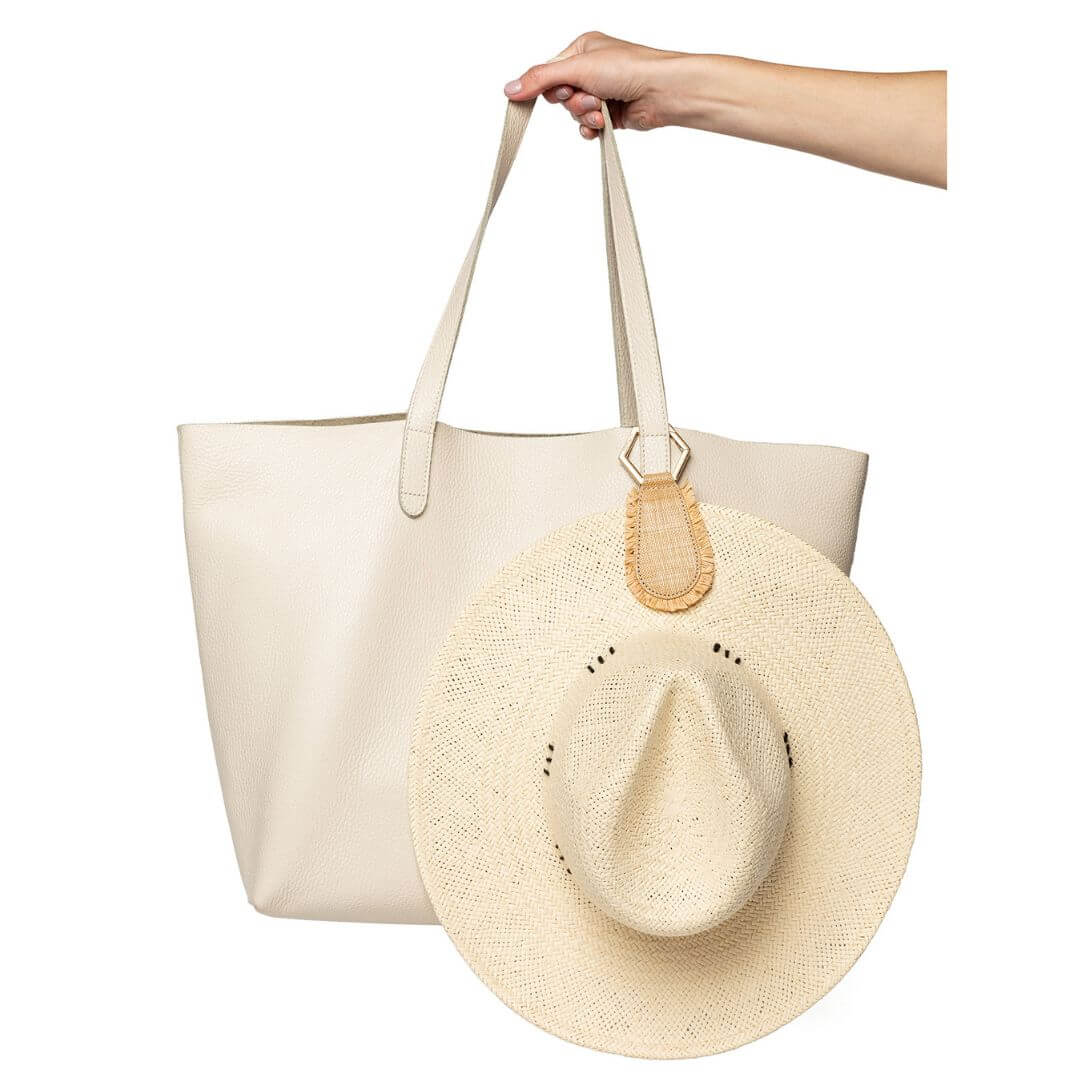 The Fray TOPTOTE Hat Clip in natural with raffia trim holding a straw hat on a beige handbag.