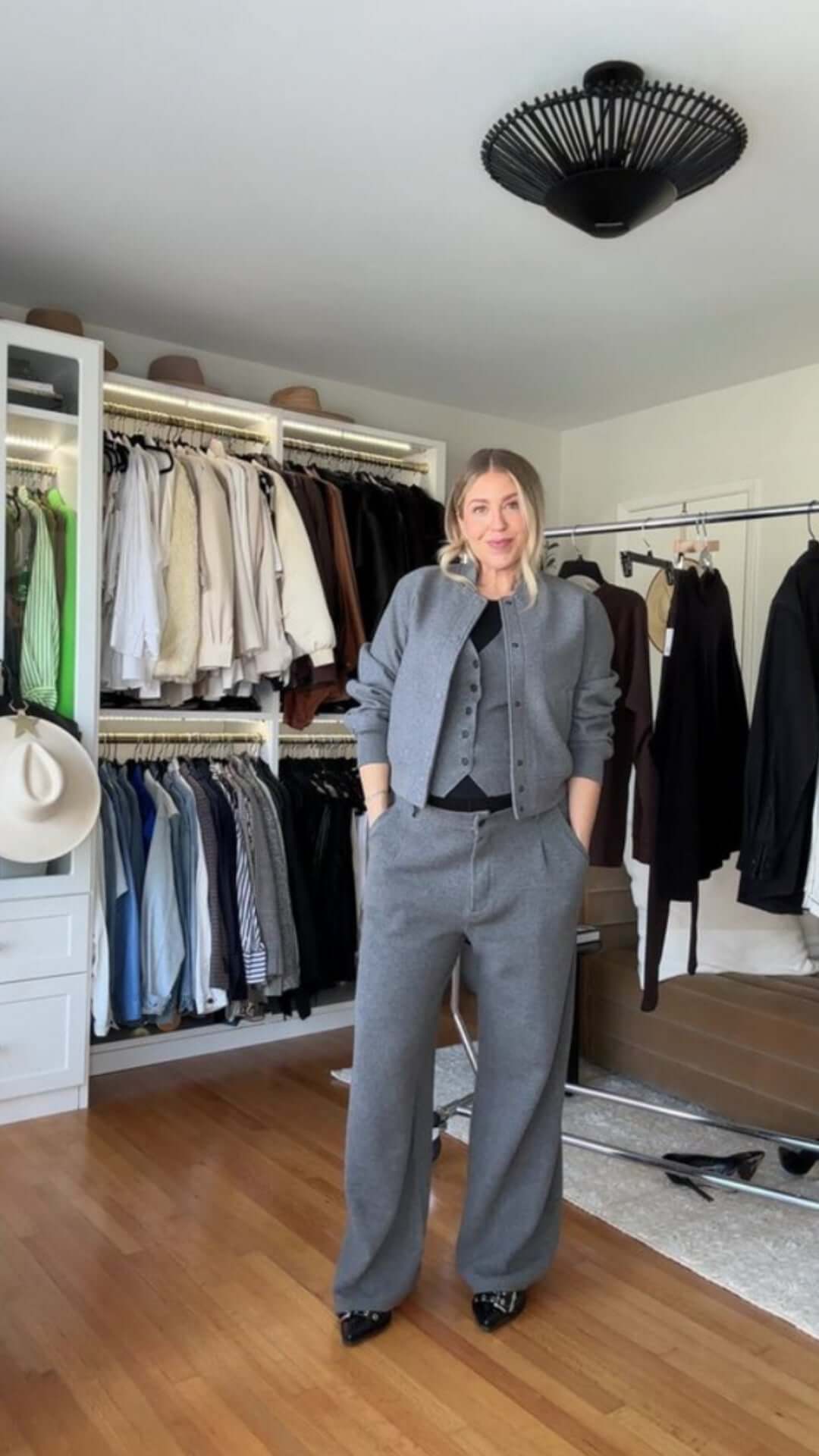 Woman in a stylish gray suit stands confidently in a well-organized wardrobe featuring a variety of clothing.