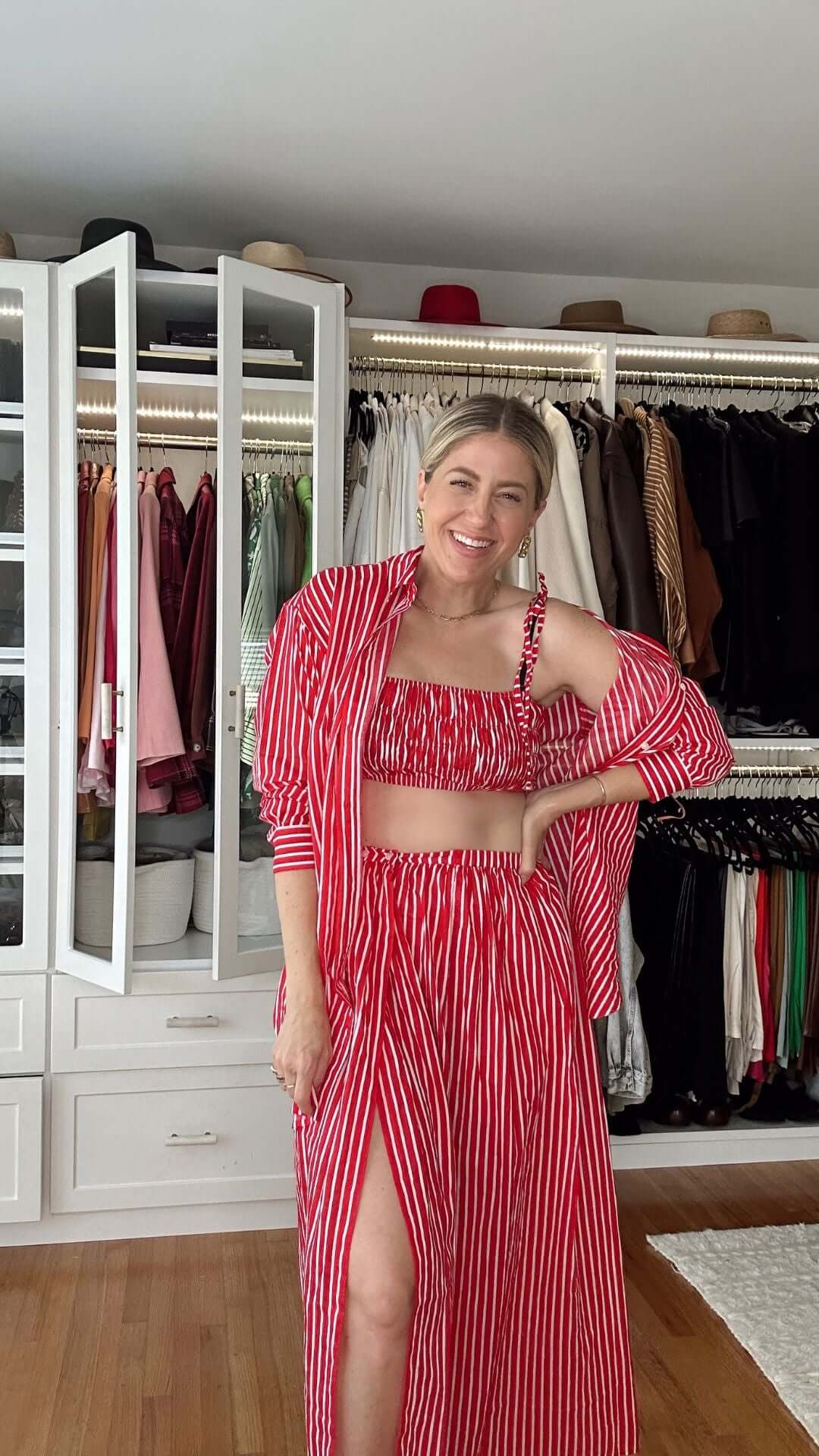 Woman in a red and white striped two-piece outfit, smiling in a stylish wardrobe setting.