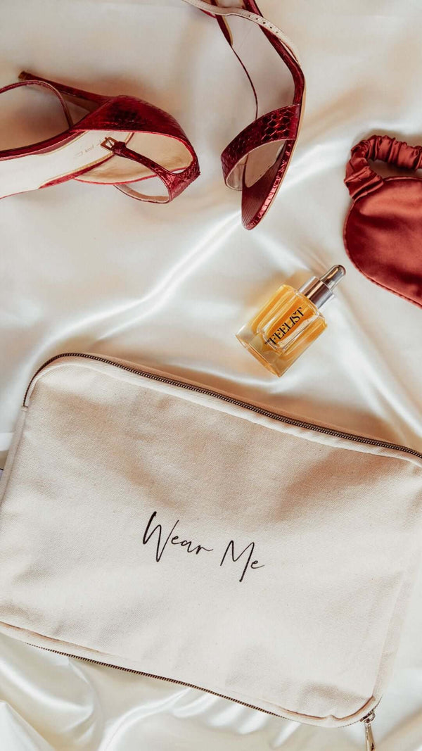 Stylish flat lay with red heels, a perfume bottle, and a makeup bag labeled 'Wear Me' on satin fabric.