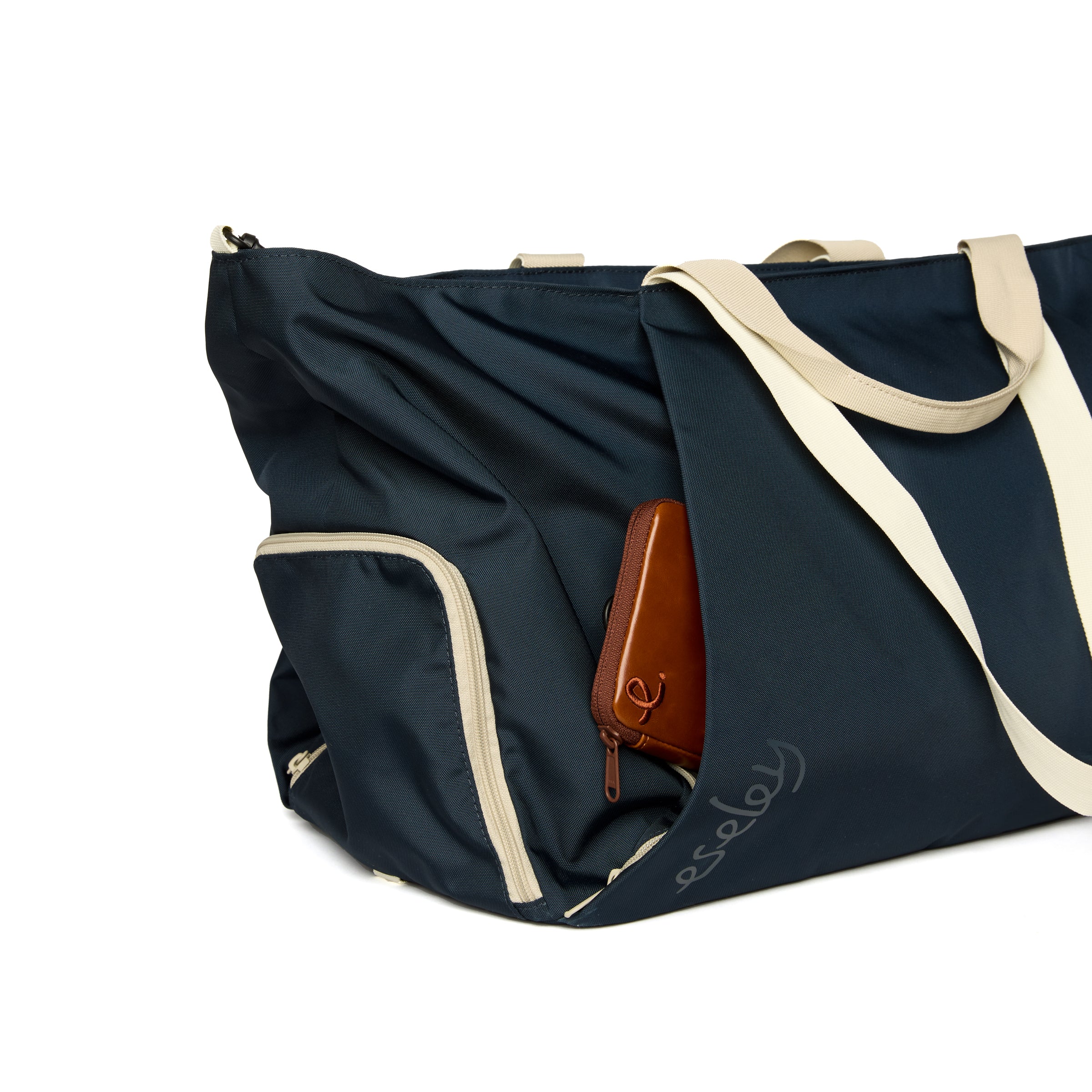 Navy duffel bag with beige straps and a brown leather wallet on a white background