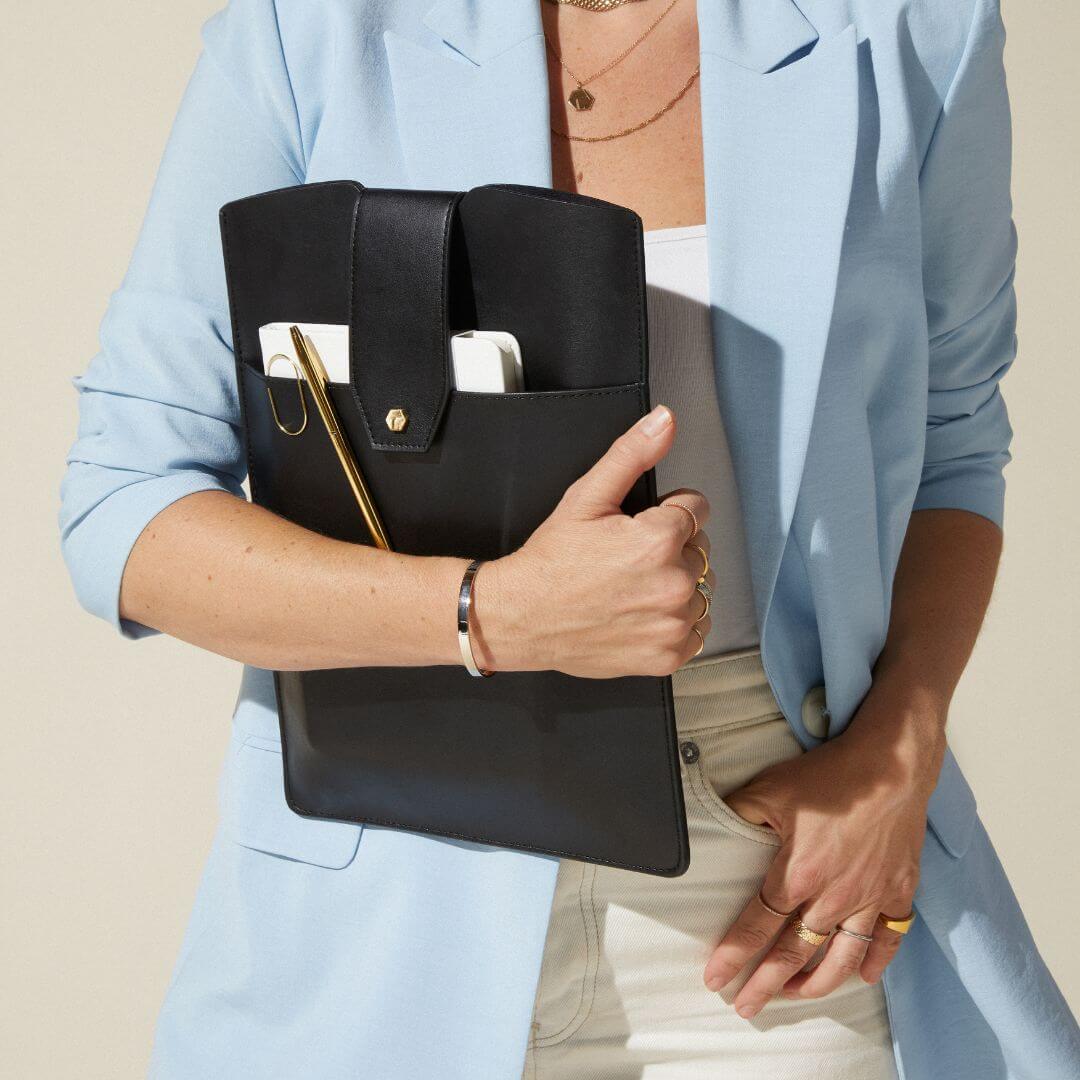 woman holding the Lindsay Albanese black daily laptop clutch with a notebook and pen tucked in the front pocket. 