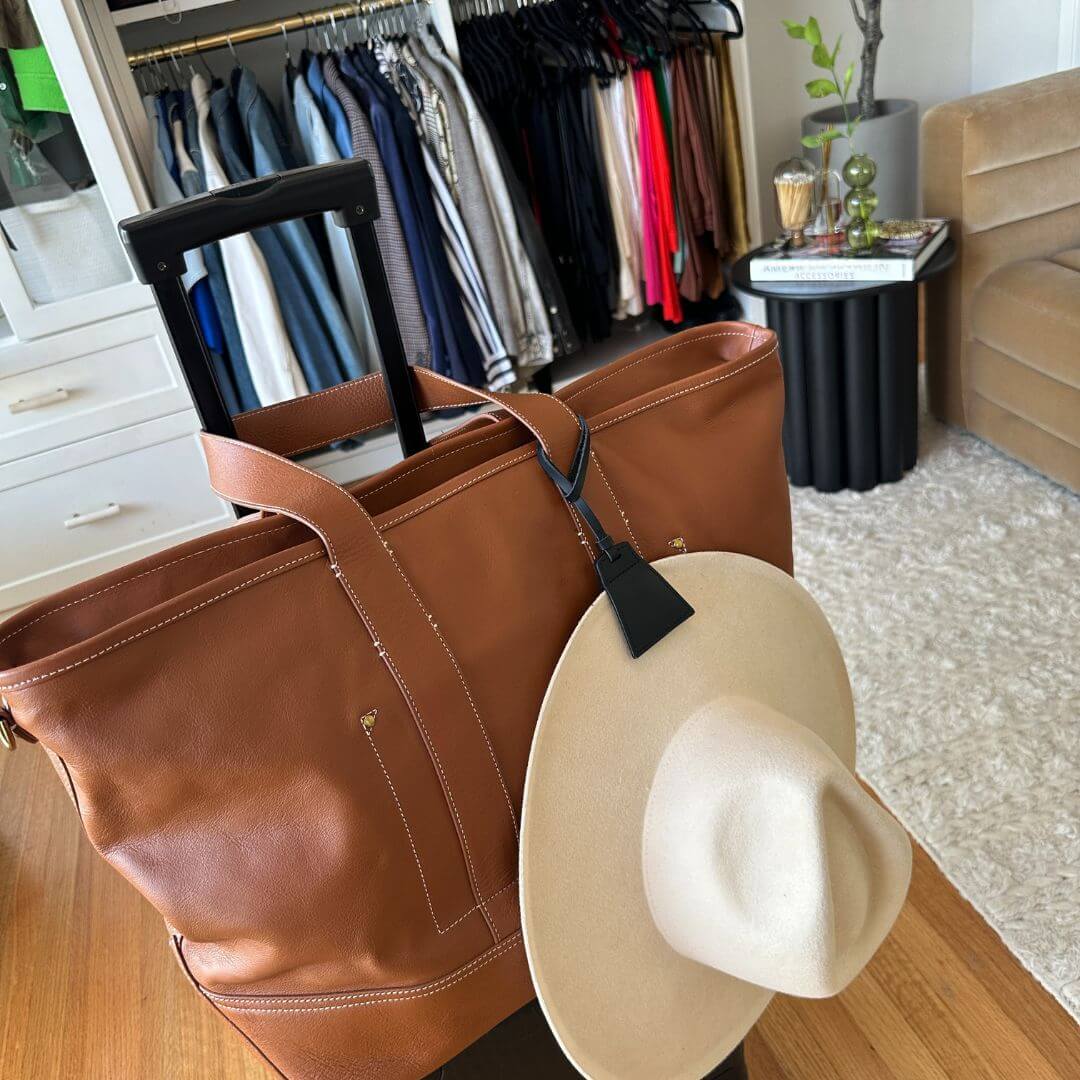 Lasso TOPTOTE hat clip holding a hat on a stylish brown handbag in a well-organized wardrobe.
