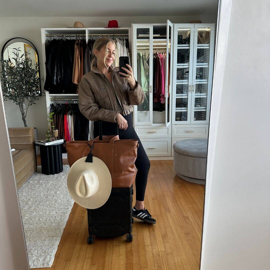 Woman taking a mirror selfie with a TOPTOTE hat clip holding a sun hat on her luggage.