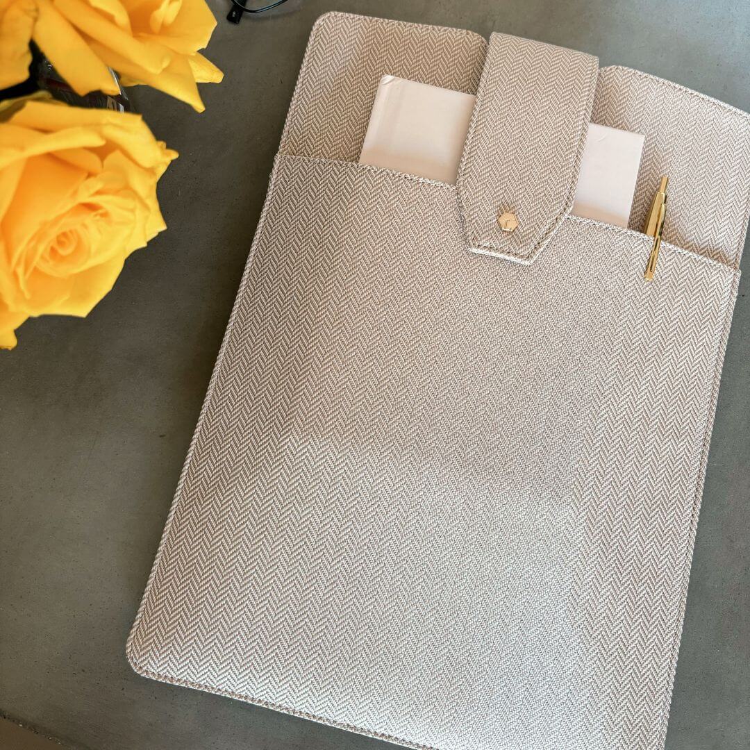 Lindsay Albanese limited edition laptop clutch, a notebook and pen tucked in the front pocket, on a table with yellow roses.
