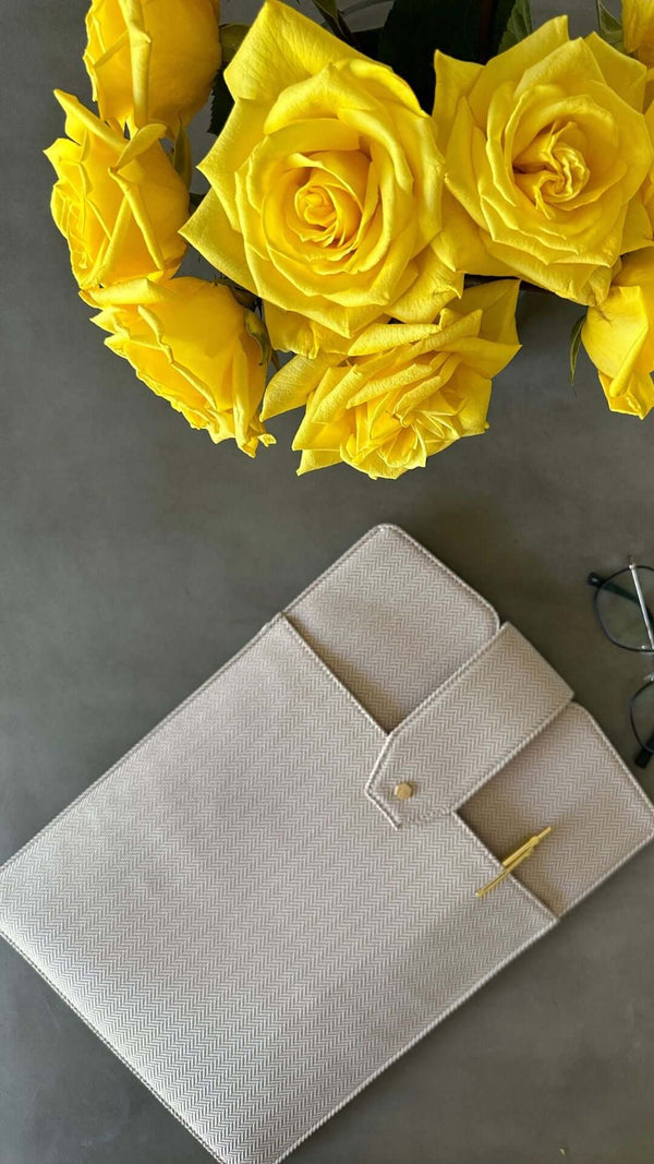Elegant arrangement of yellow roses beside a stylish beige folder on a gray surface.