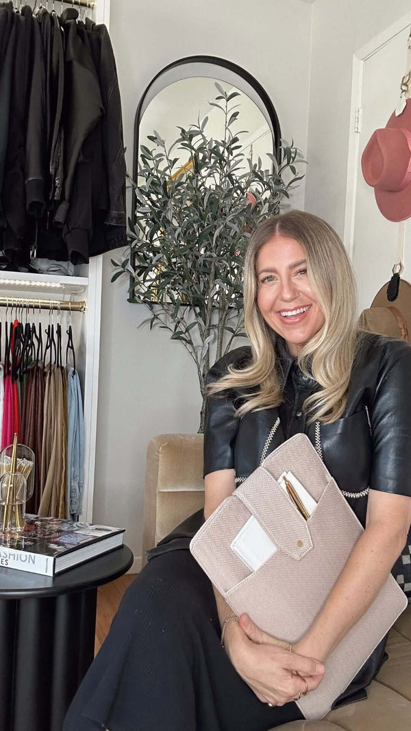 Smiling woman in stylish outfit holding a clutch in a chic fashion boutique with clothing racks.