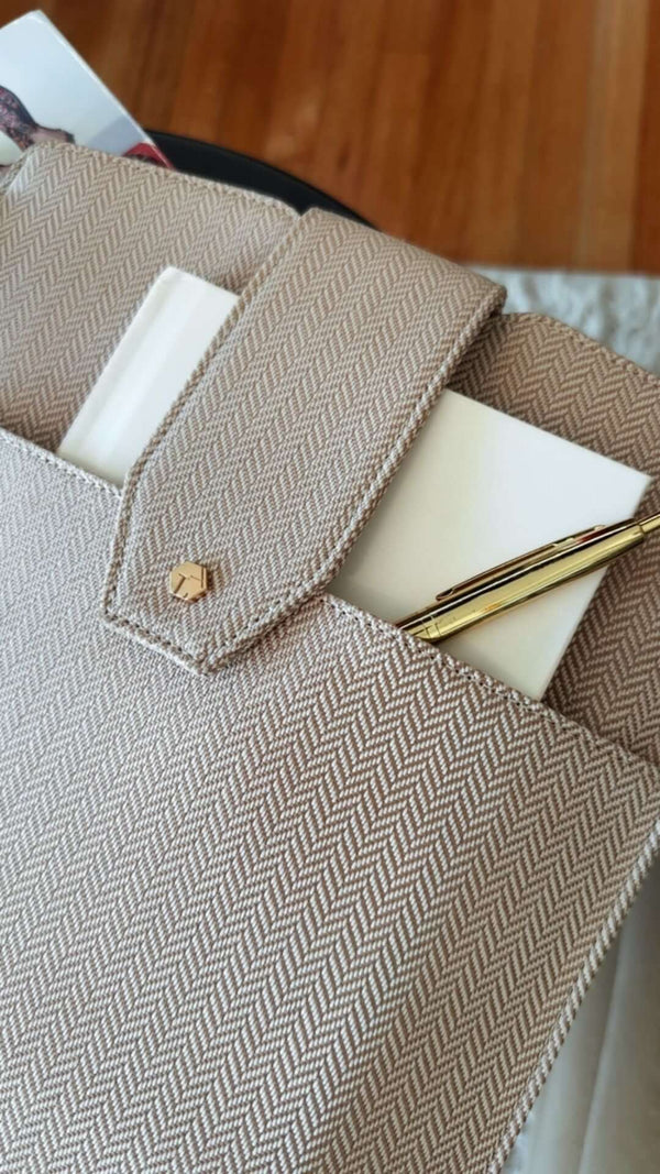 Close-up of a stylish beige herringbone bag with a notepad and pen inside, emphasizing modern workspace accessories.