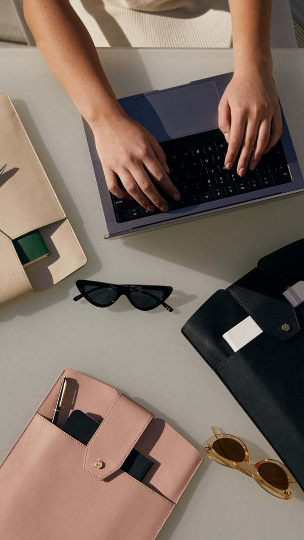 Flat lay of a workspace featuring a laptop, sunglasses, and stylish folders in pink and black.