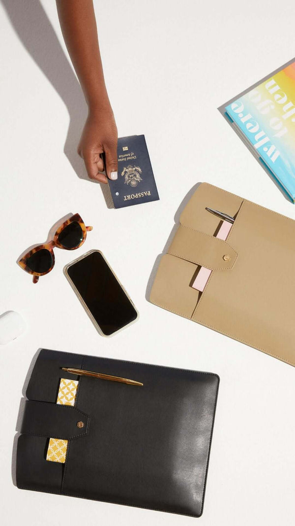 Flat lay of travel essentials including sunglasses, a smartphone, a passport, and stylish document holders.
