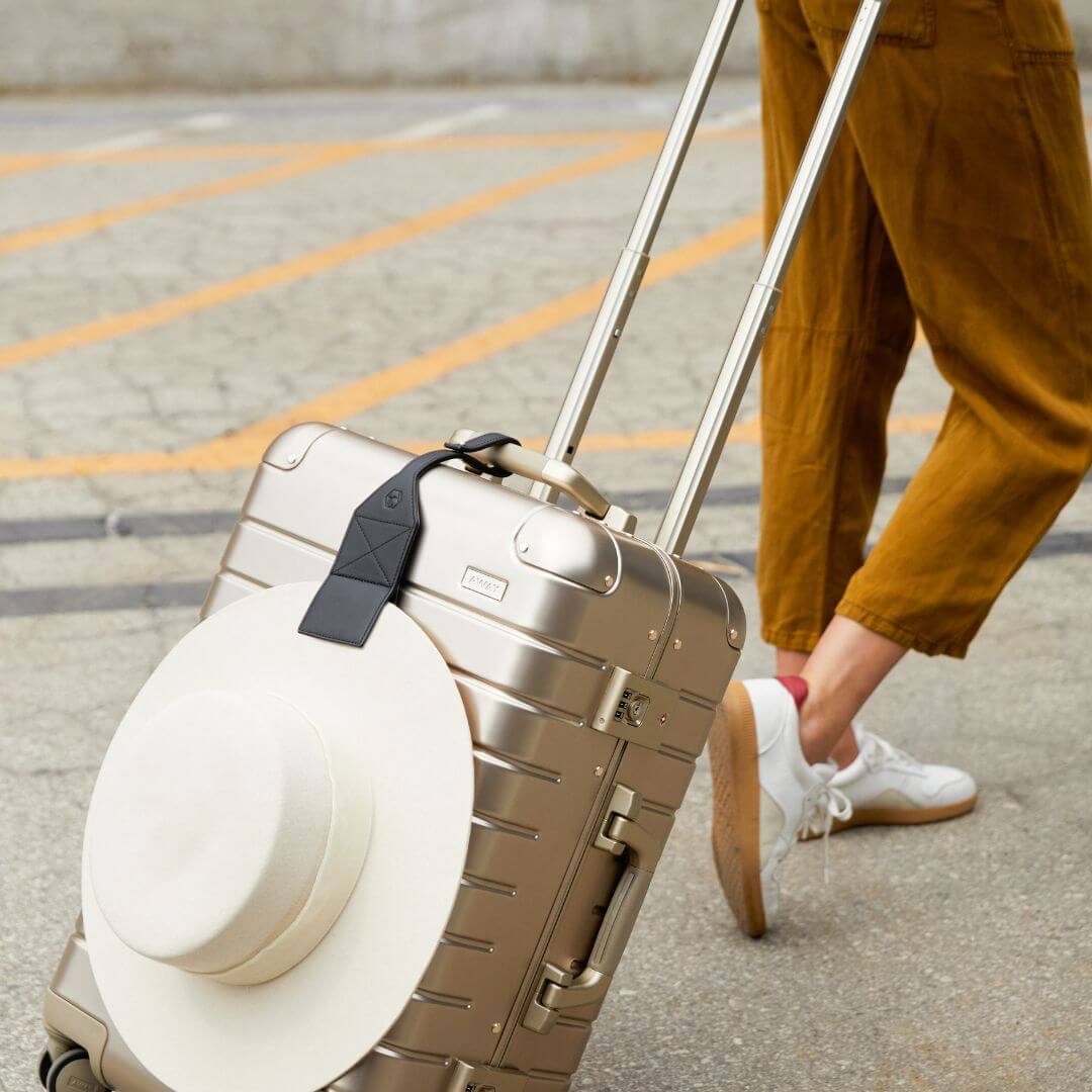 TOPTOTE black luggage clip attached to a silver suitcase holding a white hat in the city. 