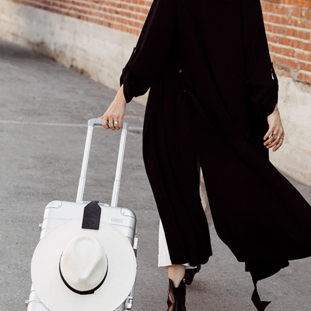 TOPTOTE black luggage clip attached to a silver suitcase holding a white hat in the city. 