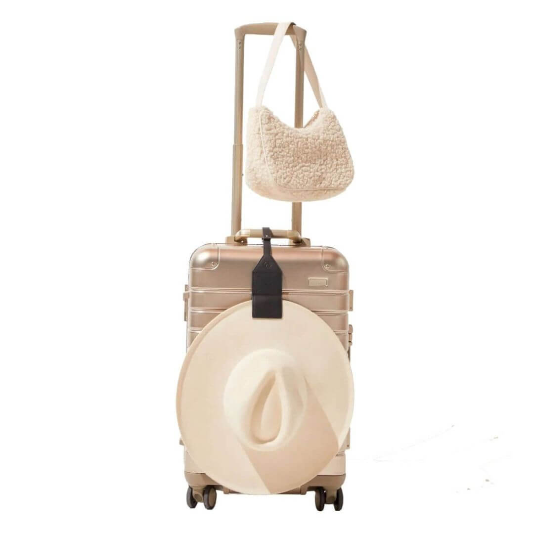 Lindsay Albanese black luggage tag TOPTOTE attached to a suitcase and holding a white hat. 