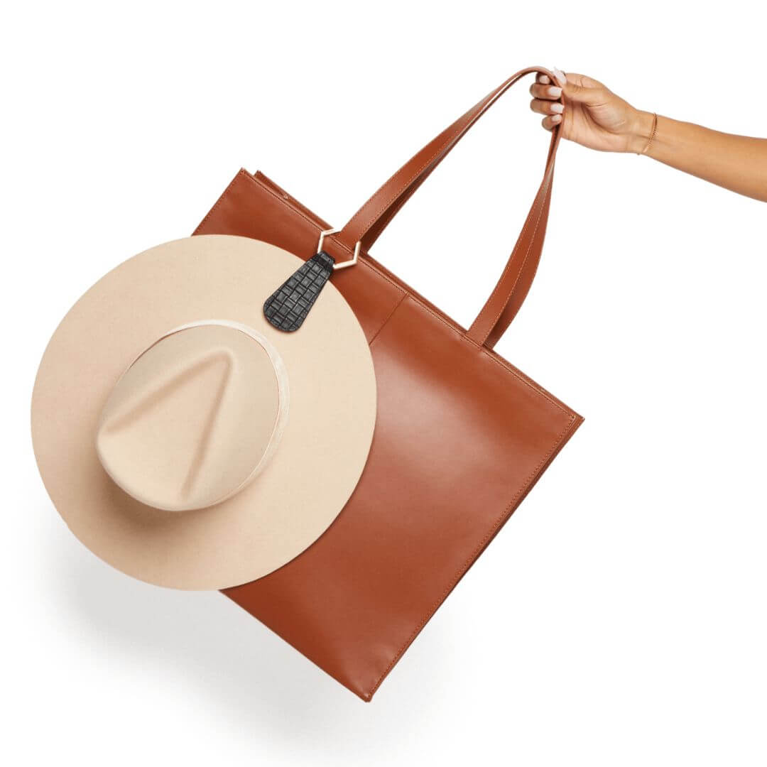 Hat attached to brown leather handbag with The Drop TOPTOTE hat clip showing hands-free travel convenience