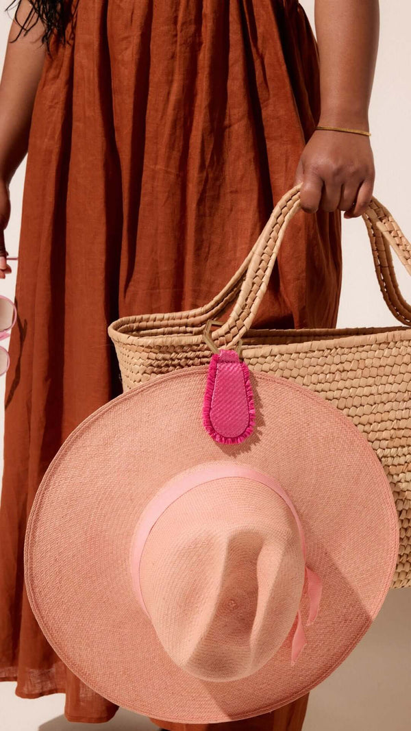 Close-up of a woman holding a straw bag and wearing a pink sun hat, styled for a summer outfit.