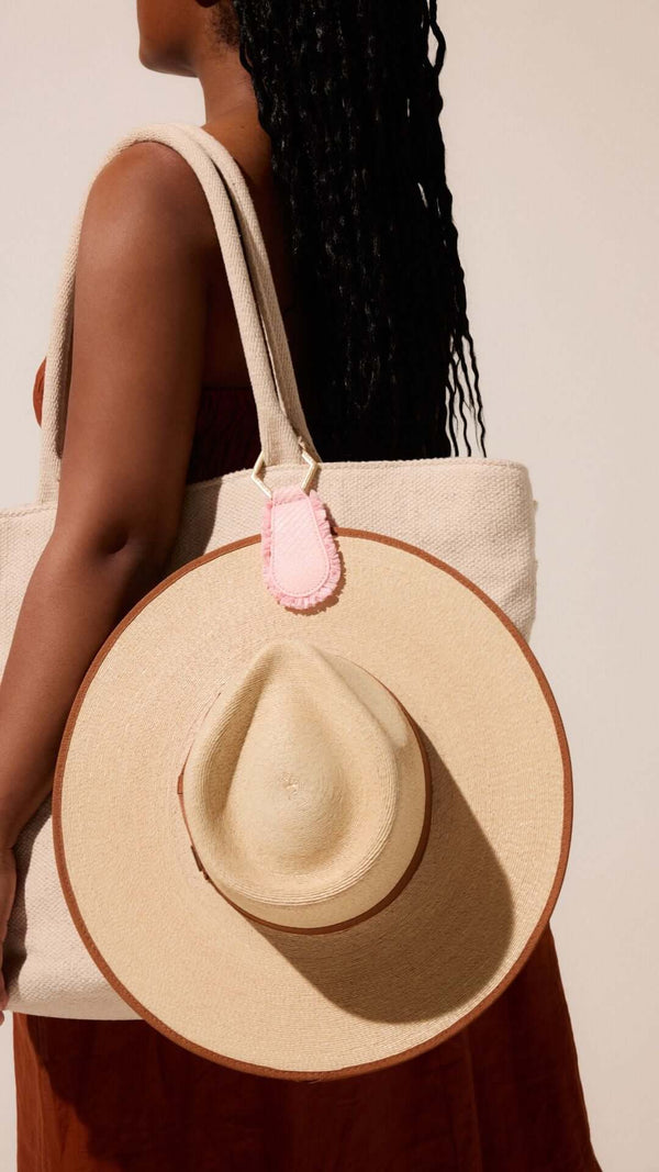 Stylish woman holding a large beige tote bag with a straw hat attached, showcasing a trendy summer look.