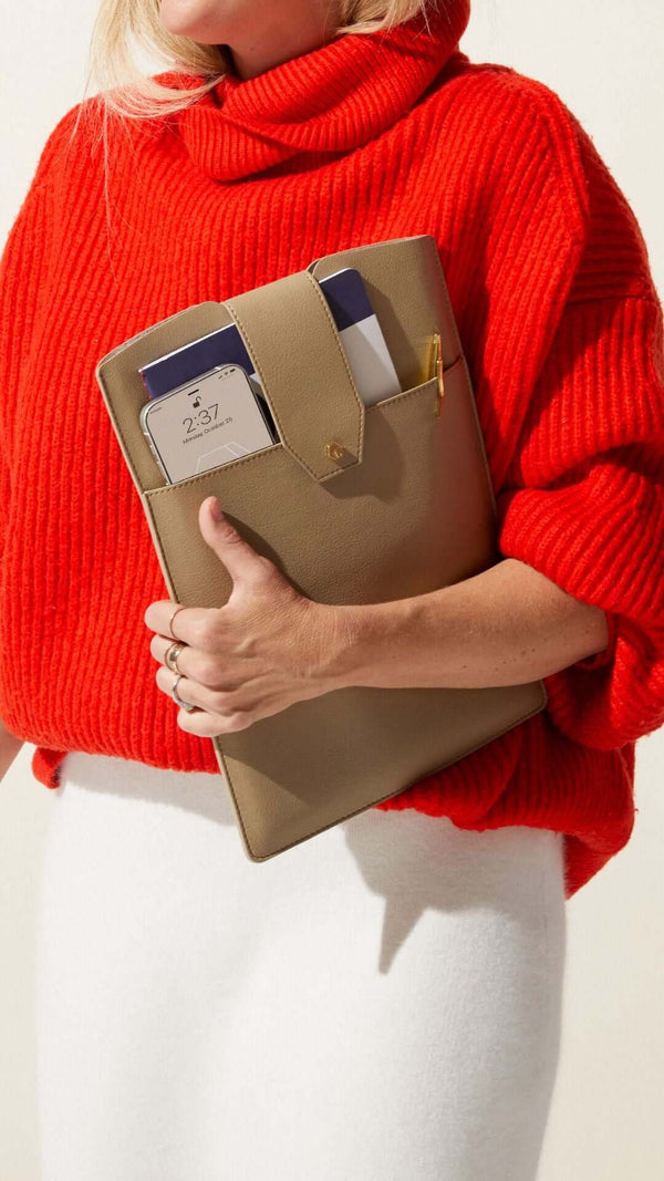 Woman wearing a cozy red sweater holding a stylish tan clutch with notebooks and a pen.