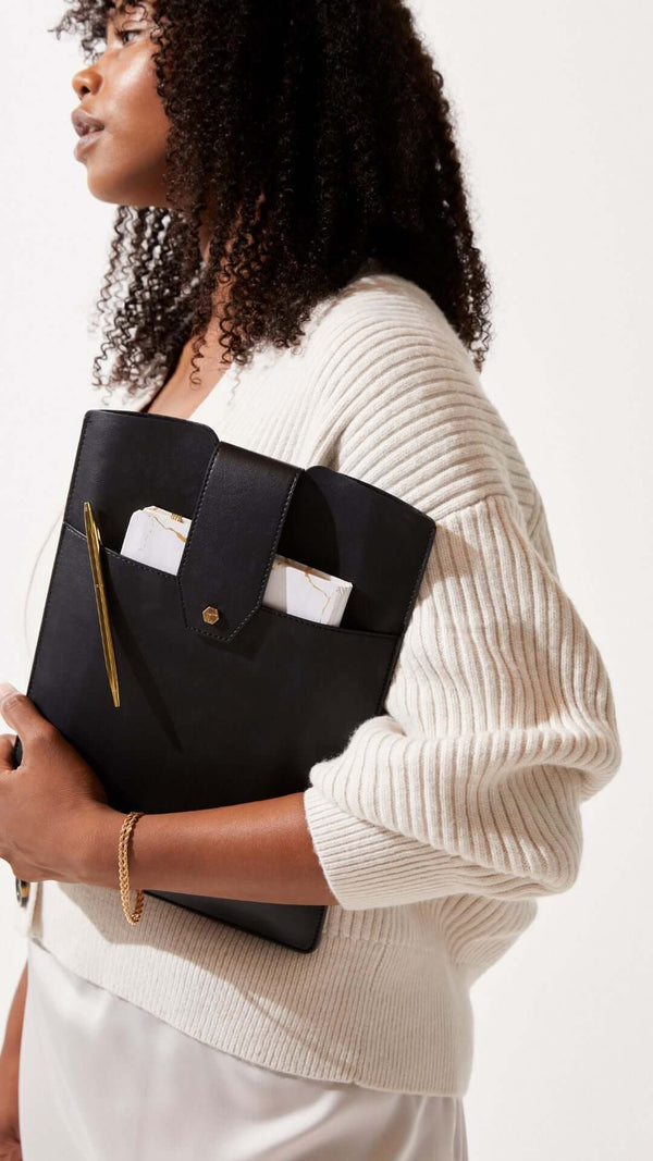 Stylish woman holding a black folder with documents, wearing a cream cable-knit sweater.