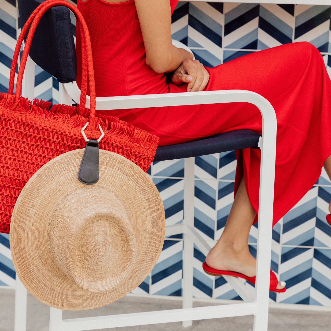 woman in a red dress sitting at a table with a red tote hanging from a chair with the faux leather black TOPTOTE hat clip attached with a cream straw hat.