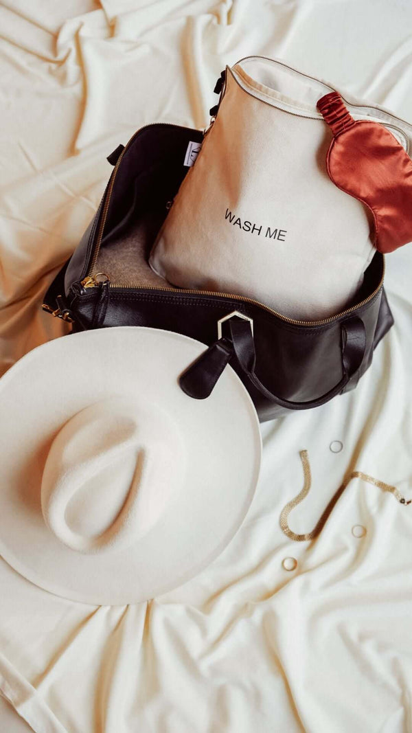 Stylish black bag with a beige wash bag and a white hat on a soft fabric background.